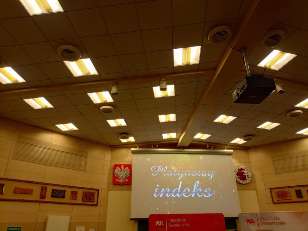 Sala wykładowa z projektorem, ekranem z napisem "Platynowy indeks" i godłem Polski.