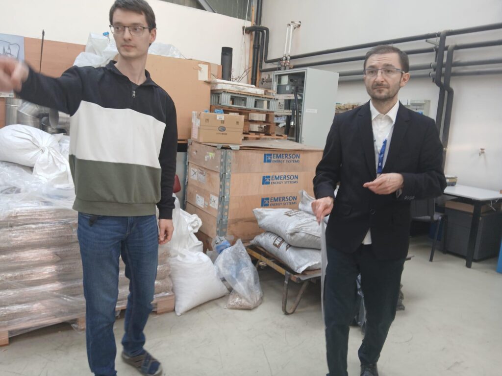 Dwóch mężczyzn stoi w magazynie. W tle widoczne są worki, palety i sprzęt.
