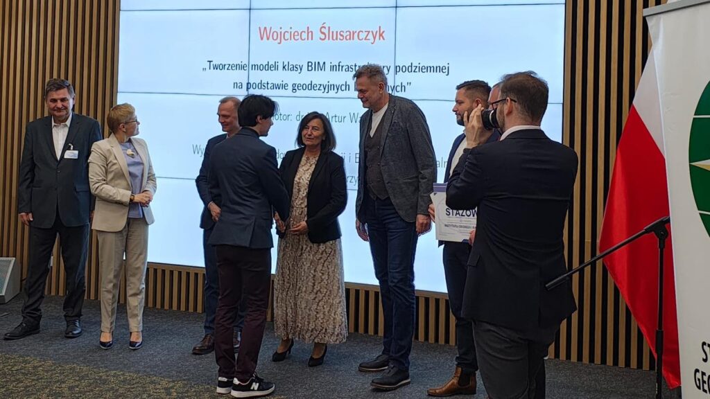Ludzie na scenie, ekran z napisem "Wojciech Ślusarczyk", polska flaga. Kontekst: wydarzenie branżowe.