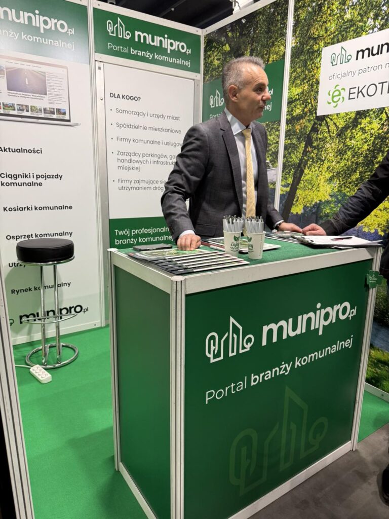 Mężczyzna w garniturze przy stoisku z zielonymi panelami i logo "munipro.pl". Kontekst: targi branżowe.