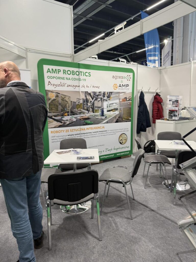 Stoisko targowe z robotyką AMP Robotics. W tle zielony baner z logo i hasłem. Widać fragmenty robotów.