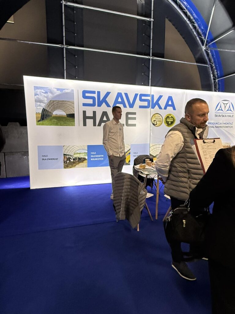 Stoisko firmy Skavska Hale. W tle baner z logo i zdjęciami hal. W centrum mężczyźni w strojach firmowych.