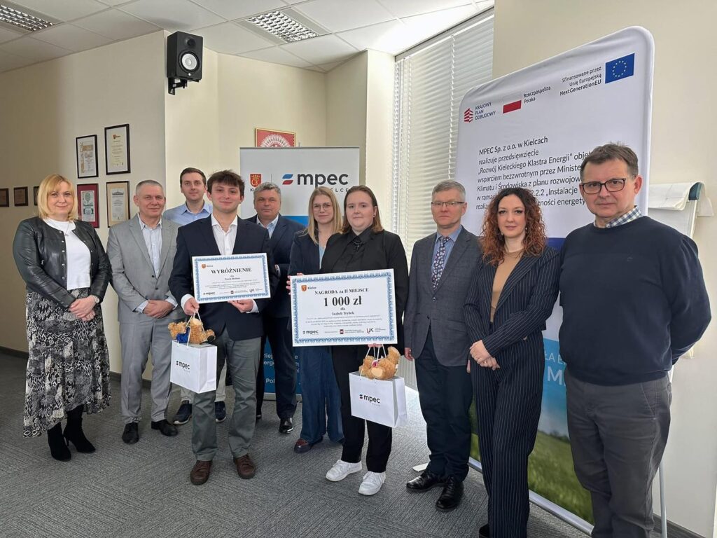 Grupa osób pozuje do zdjęcia z certyfikatami i torbami. W tle baner MPEC Sp. z o.o. w Kielcach.