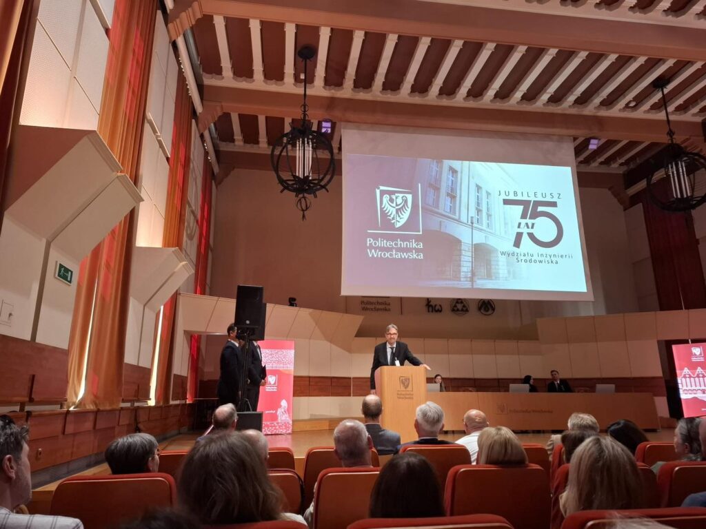 Mężczyzna przemawia na scenie przed ekranem z napisem "Jubileusz 75 lat Politechniki Wrocławskiej".