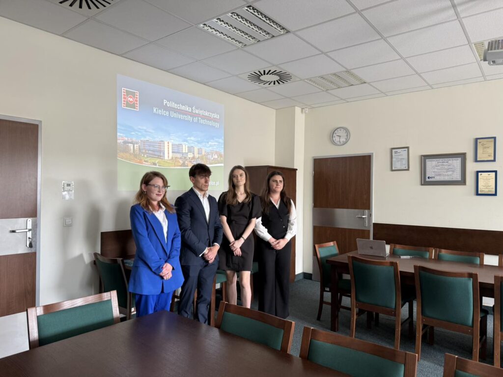Cztery osoby stoją przed ekranem z logo Politechniki Świętokrzyskiej. W sali konferencyjnej znajdują się stoły i krzesła.