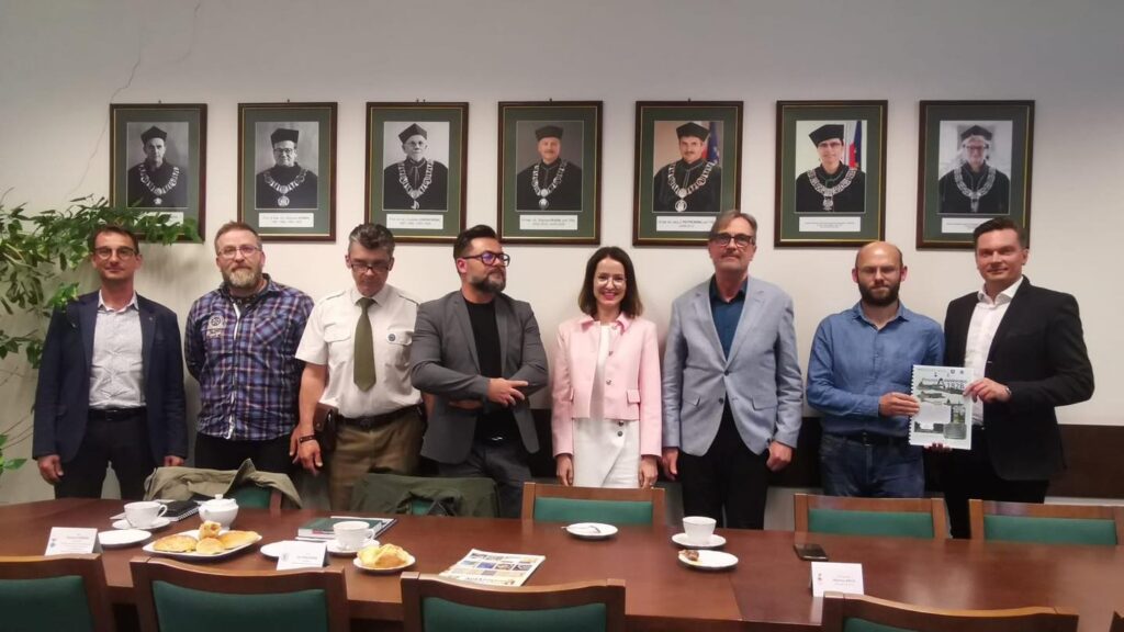 Grupa osób stoi przed portretami w togach. Na stole są przekąski i napoje.