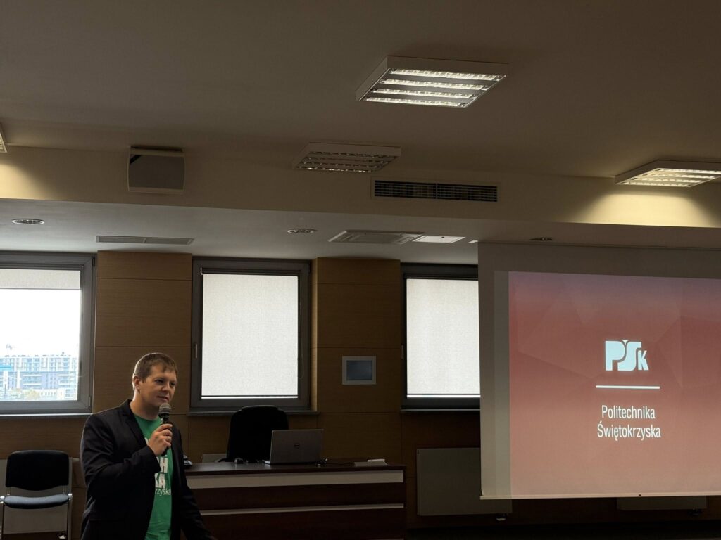 Mężczyzna w garniturze i zielonej koszulce mówi do mikrofonu. Na ekranie logo Politechniki Świętokrzyskiej.
