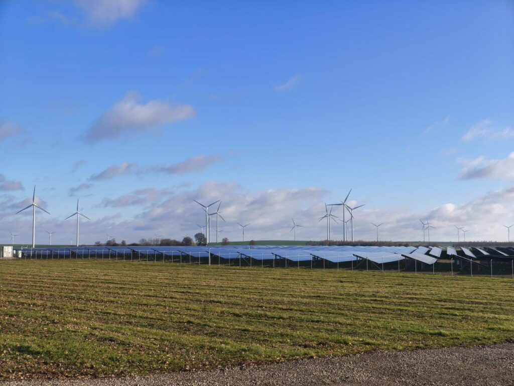 Wiatraki i panele słoneczne na tle błękitnego nieba. Farma wiatrowa i słoneczna.