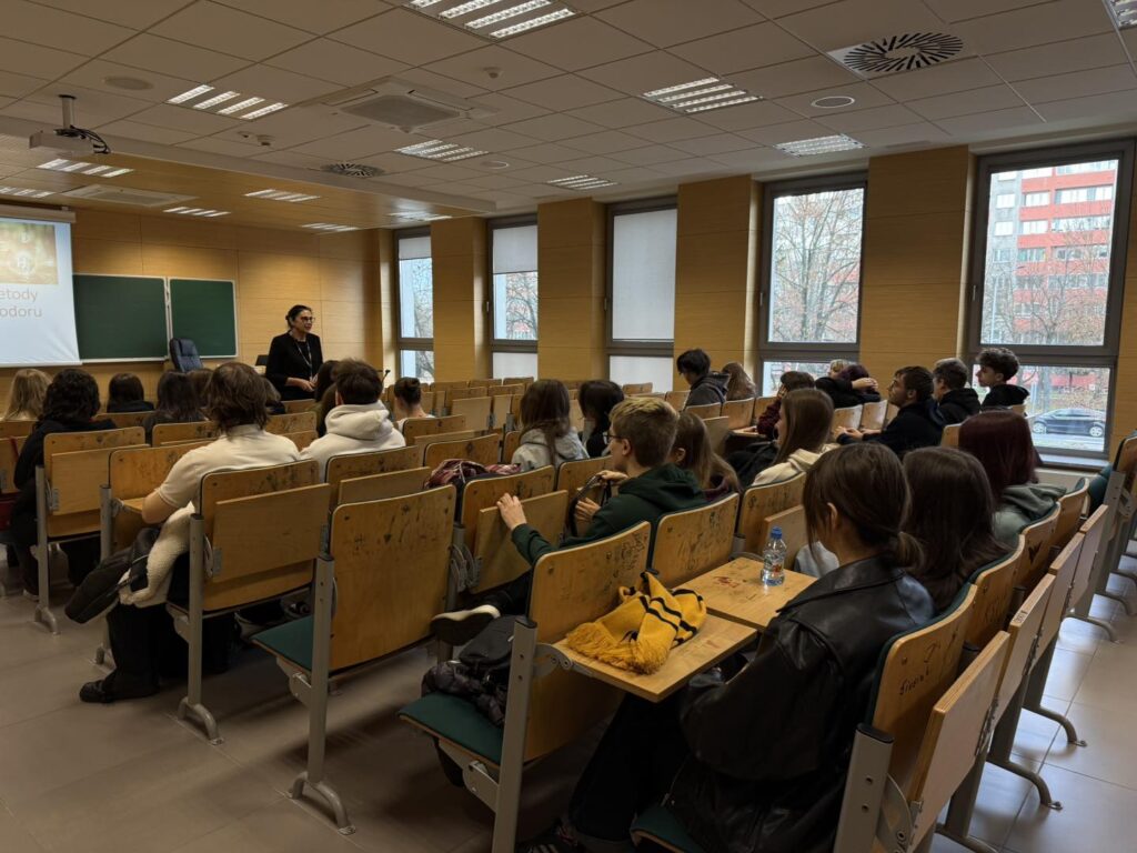 Nauczycielka prowadzi lekcję dla grupy studentów siedzących w sali wykładowej.