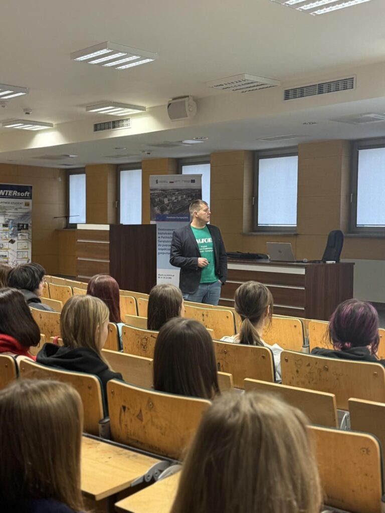 Mężczyzna w zielonej koszulce przemawia do studentów siedzących w sali wykładowej.