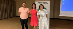 Trzy osoby stoją przed banerem "Stowarzyszenie Geodetów Polskich". W tle ekran projekcyjny.