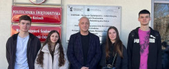 Cztery osoby stoją przed budynkiem Politechniki Świętokrzyskiej. W tle tablice informacyjne i godło Polski.