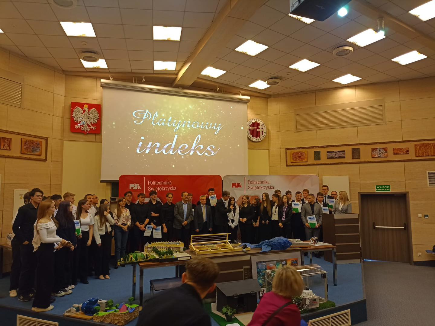 Grupa studentów i wykładowców na scenie. Na ekranie napis "Platynowy indeks".
