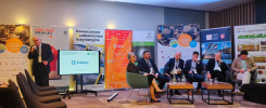 Panel dyskusyjny na konferencji budowlanej. Uczestnicy siedzą przy stołach, jeden mężczyzna przemawia.