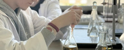 Młody mężczyzna w fartuchu laboratoryjnym wykonuje eksperyment. Kluczowe obiekty: kolby, płyny, fartuchy.