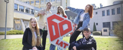 Pięć osób pozuje z dużym czerwono-białym logo "60 LAT" przed budynkami.