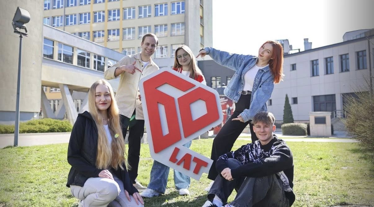 Pięć osób pozuje z dużym czerwono-białym logo "60 LAT" przed budynkami.