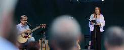 Mężczyzna gra na gitarze, kobieta czyta z książki. W tle neonowy napis "Pataczyk Zielińskiego". Koncert.
