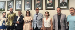 Grupa osób pozuje do zdjęcia na tle portretów. W kadrze: 4 kobiety, 4 mężczyzn, portrety.