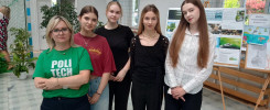Grupa osób stoi przed tablicami edukacyjnymi. Kluczowe obiekty: kobiety, tablice, rośliny.