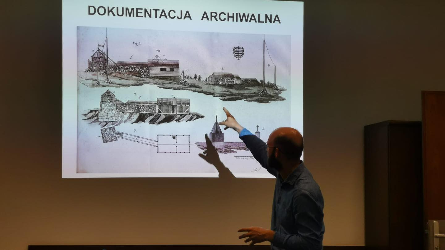 Prezentacja archiwalna z rysunkami budowli. Mężczyzna wskazuje na ekran.