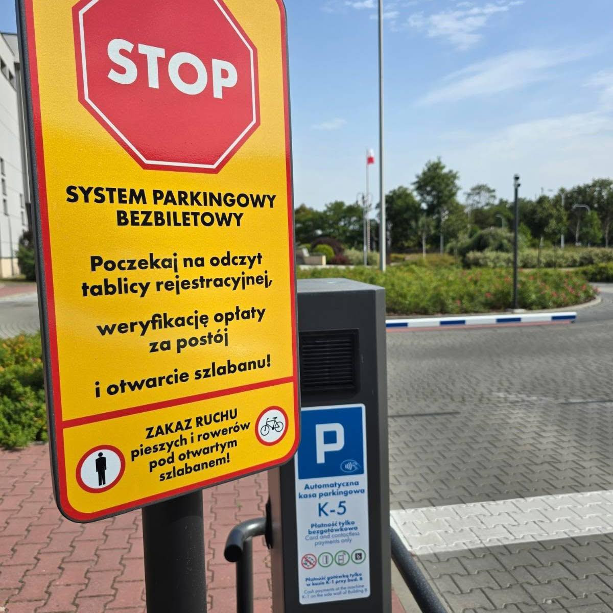Znak informuje o systemie parkingowym bezbiletowym. Kluczowe obiekty: znak STOP, kasa parkingowa, szlaban.