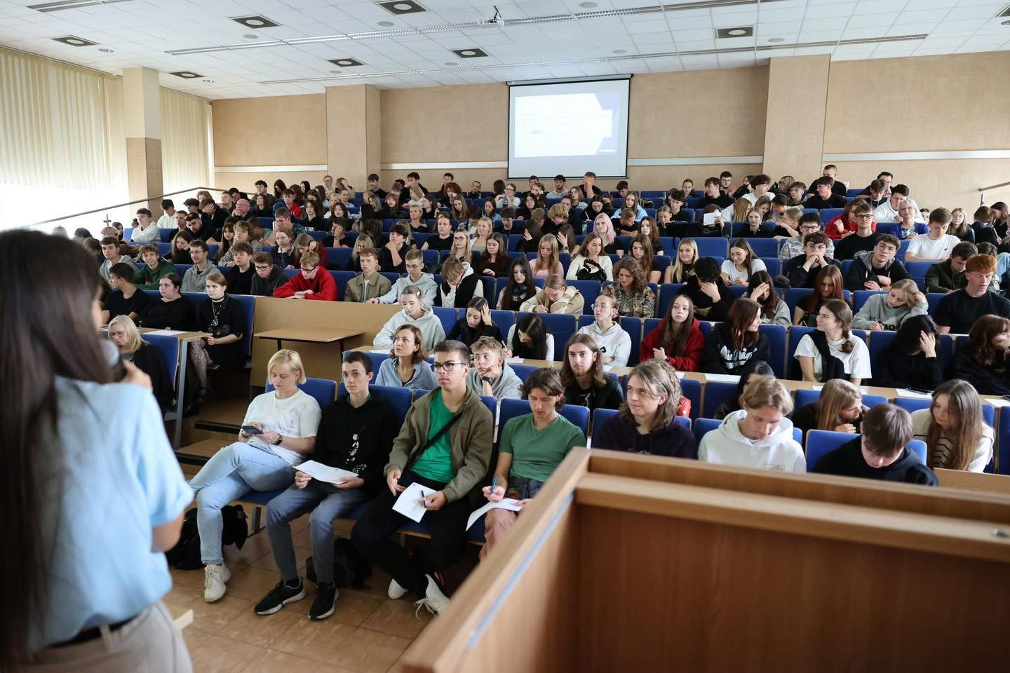 Wykład w auli uniwersyteckiej. Studenci siedzą w rzędach, słuchając wykładowcy.
