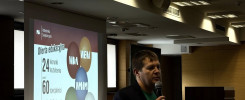 Mężczyzna z mikrofonem przemawia na tle prezentacji o ofercie edukacyjnej Politechniki Świętokrzyskiej.
