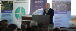 Mężczyzna przemawia na tle banerów "geo connect expo", "Stowarzyszenie Geodetów Polskich" i "Fundusze Europejskie".