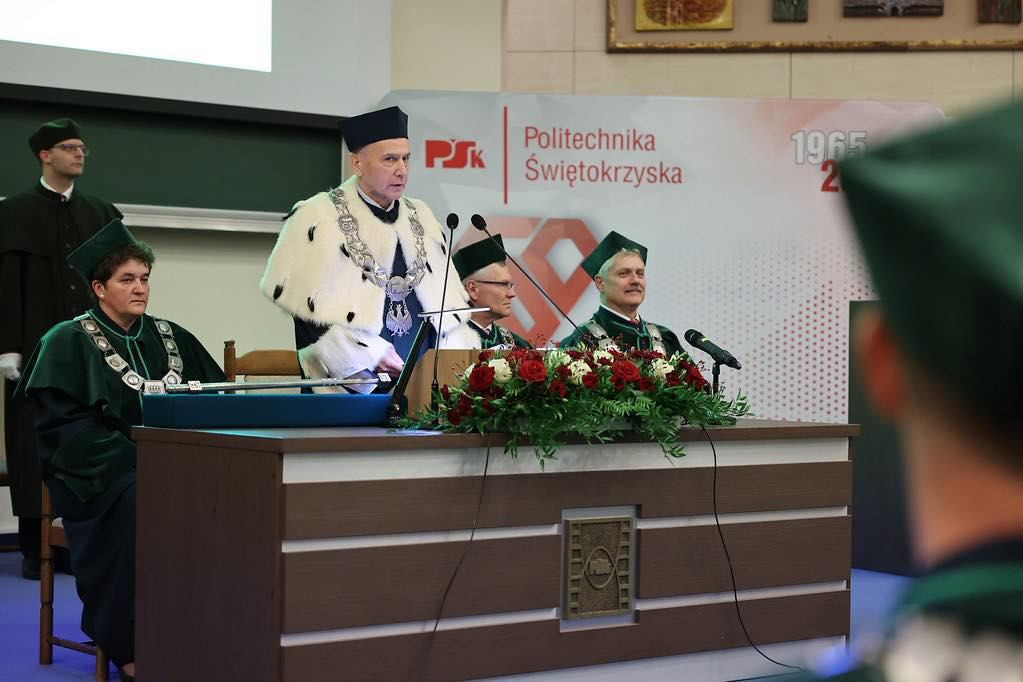 Uroczystość na Politechnice Świętokrzyskiej. Kluczowe obiekty: osoby w togach, kwiaty, podium.