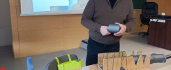Mężczyzna prezentuje materiały izolacyjne. Na stole znajdują się narzędzia, próbki materiałów i przyrząd do cięcia.