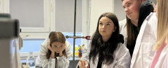 Uczniowie w fartuchach laboratoryjnych wykonują eksperyment. Kluczowe obiekty: kolby, zlewki, biureta, menzurka.