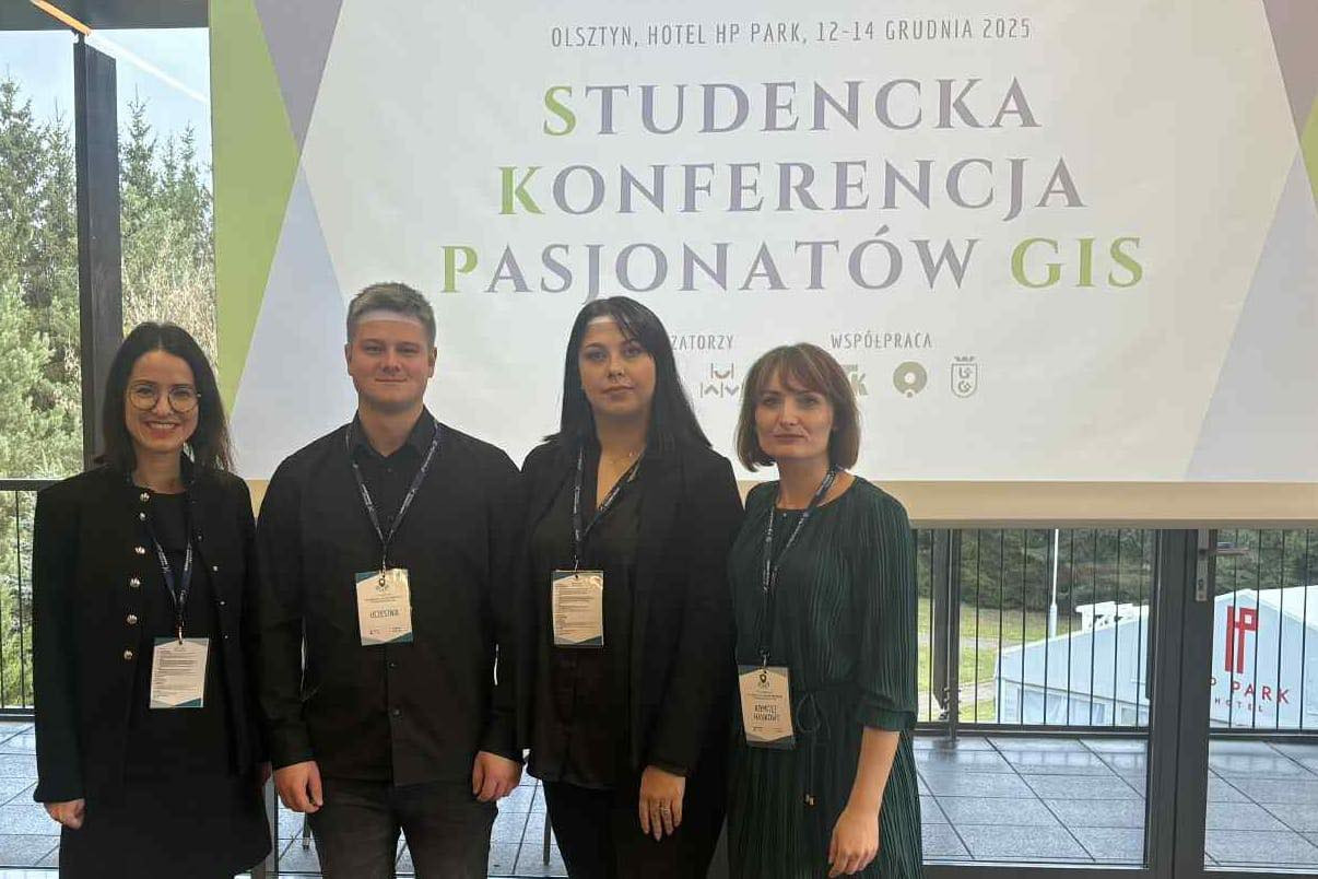 Cztery osoby stoją przed banerem konferencji "Studencka Konferencja Pasjonatów GIS" w Hotelu HP Park w Olsztynie.