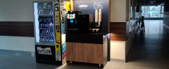 Automat z napojami i ekspres do kawy Lavazza stoją w korytarzu. Kluczowe obiekty: automat, ekspres, Lavazza, DrWitt.