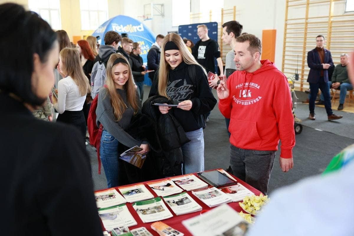 Ludzie przy stole z materiałami informacyjnymi. W tle niebieski namiot.