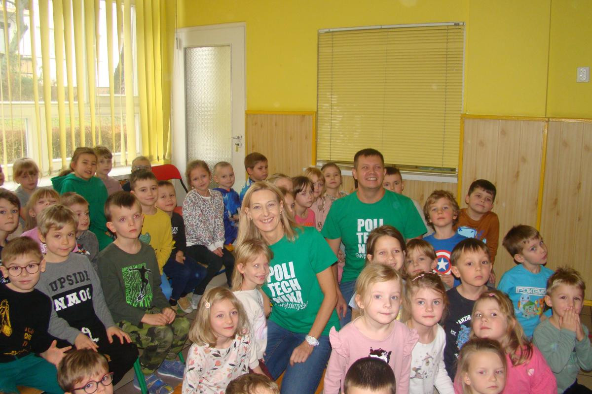 Grupa dzieci i dwoje dorosłych w zielonych koszulkach z napisem "POLI TECH". Kontekst: wydarzenie lub spotkanie.
