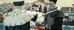 Uroczystość akademicka. Dwóch mężczyzn w togach i biretach. Jeden przekazuje drugiemu berło.